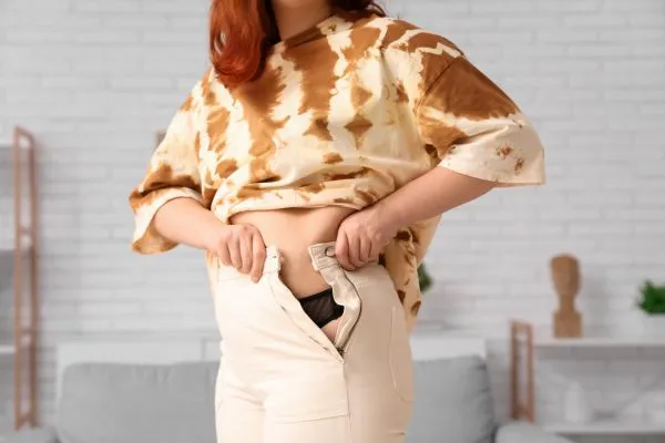 Image of woman trying to do her trousers up after pregnancy weight gain Hungerford